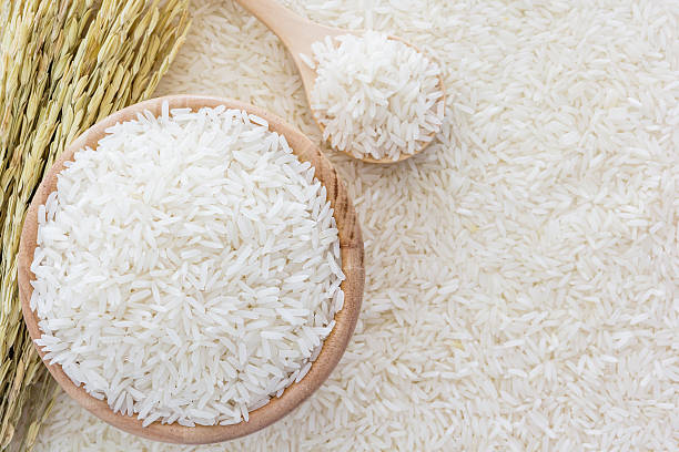 White rice in bowl and a bag, a wooden spoon and rice plant on white rice background, Top view with copy space